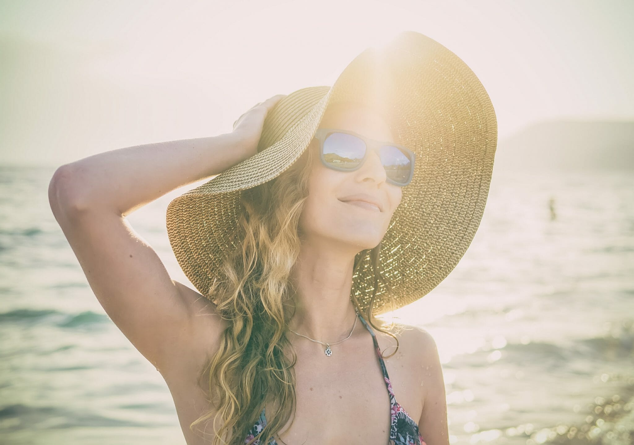 Young blondy girl in sunglasses and straw hat at the beach