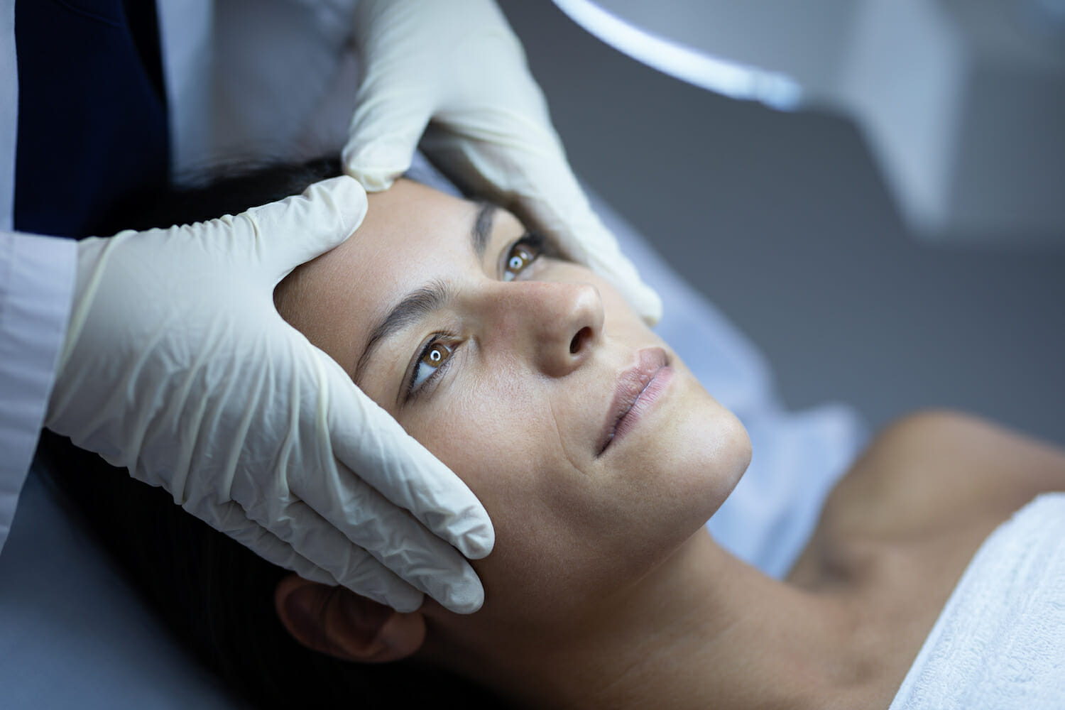 Side view of a female surgeon examining her Caucasian patient during plastic surgery in clinic