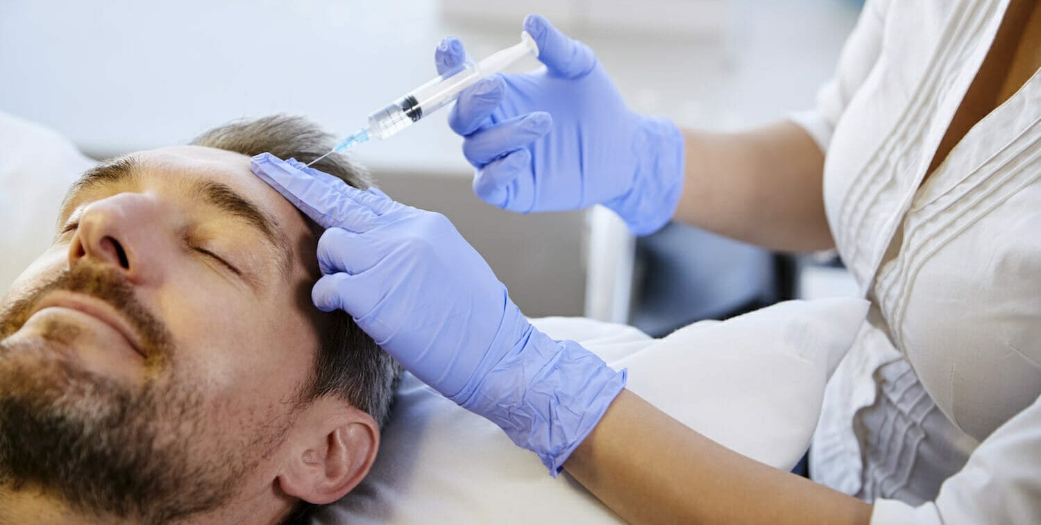 Female Beautician Giving Mature Male Patient Botox Injection In Forehead