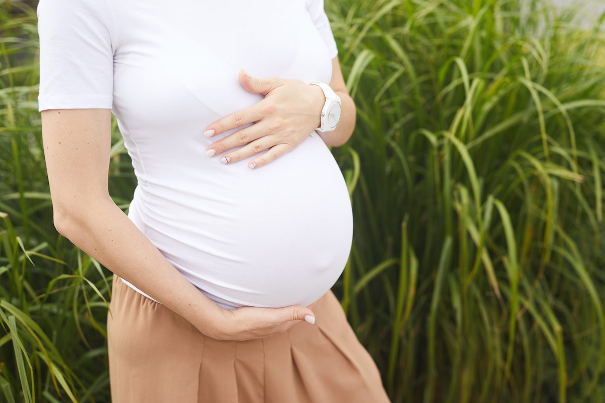 young pregnant woman standing in a field of tall grass