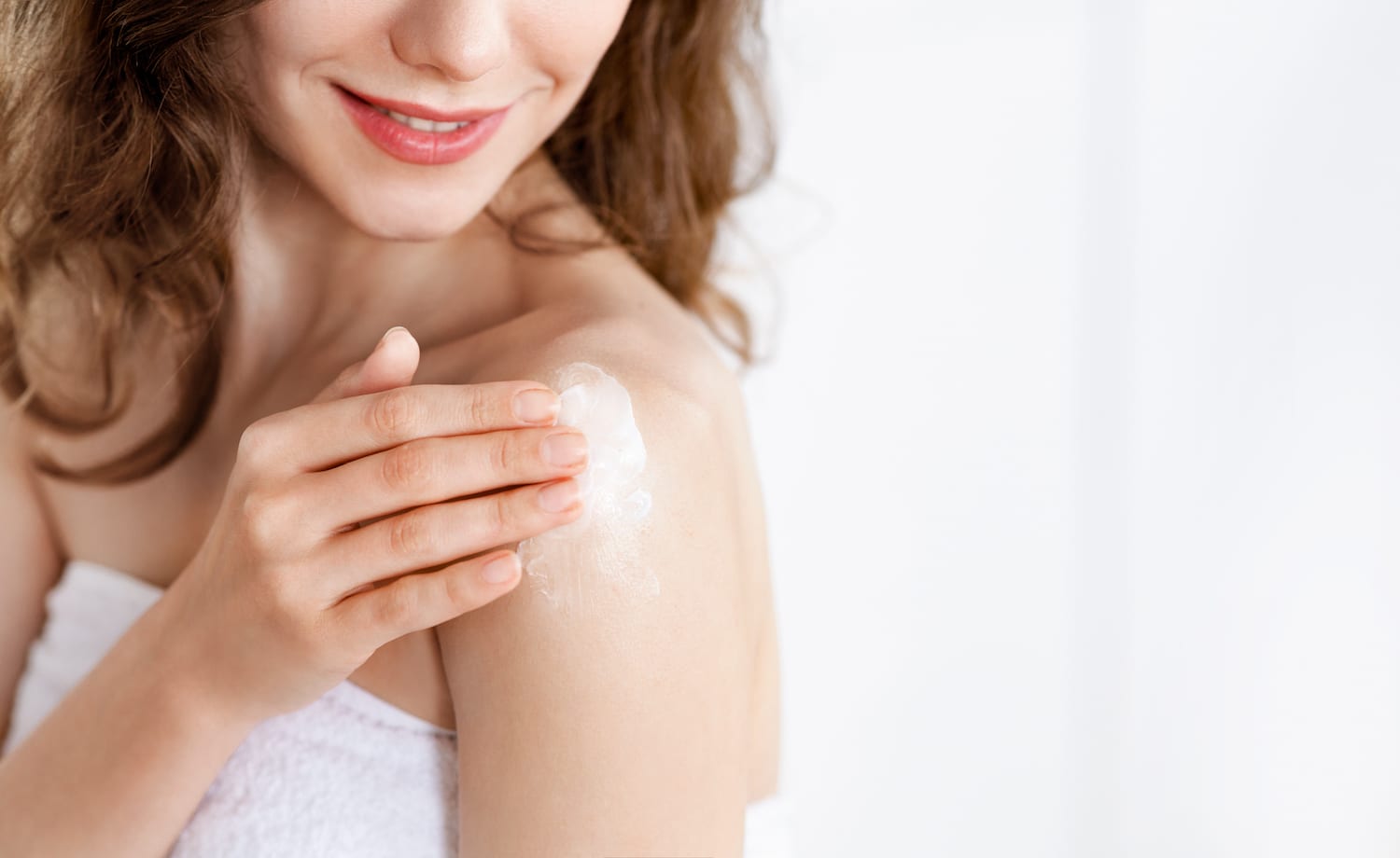 brunette woman in a towel applying lotion to her shoulder