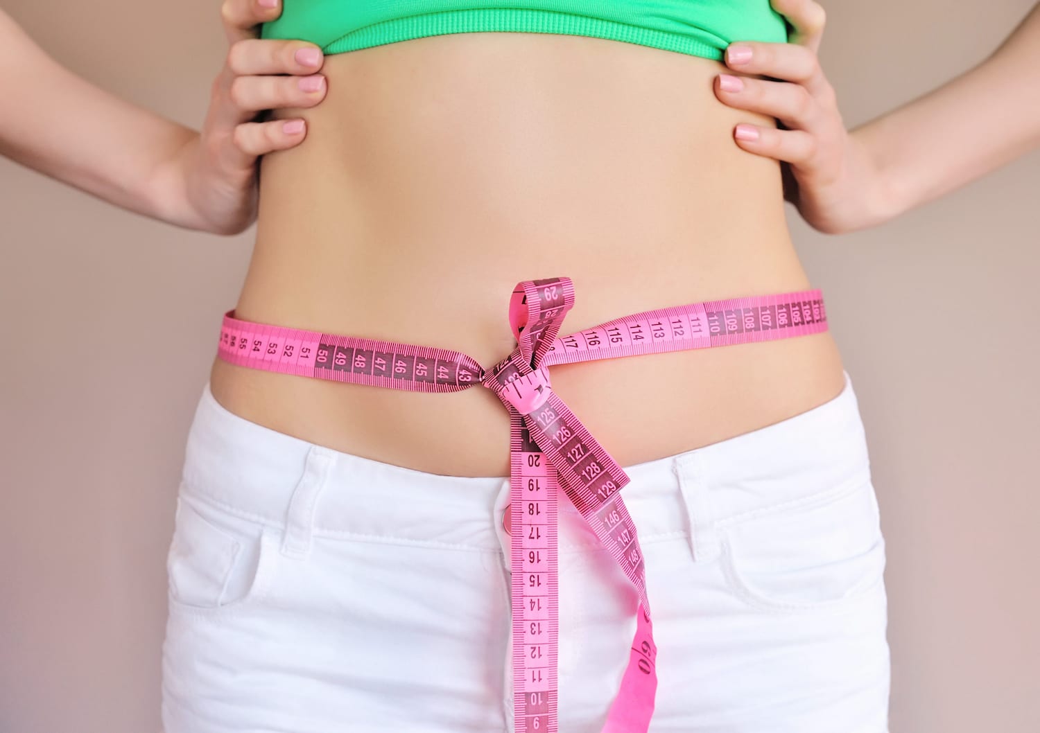 slim woman with a pink tape measure tied neatly around her stomach